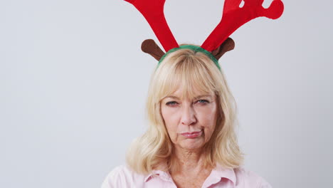 Studio-Shot-Of-Unhappy-Mature-Woman-Wearing-Dressing-Up-Reindeer-Antlers-Against-White-Background