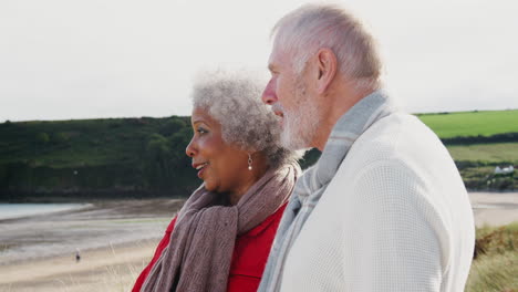 Active-Senior-Couple-Looking-Out-Over-Beach-As-They-Walk-Along-Coastal-Path-In-Fall