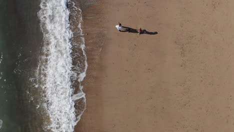 Drone-Shot-Of-Family-On-Vacation-With-Father-And-Children-Walking-Along-Beach-By-Breaking-Waves