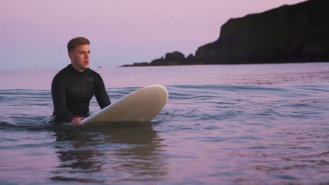 Man-Wearing-Wetsuit-Sitting-And-Floating-On-Surfboard-On-Calm-Sea