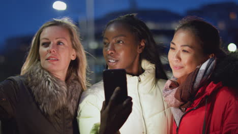 Group-Of-Female-Friends-On-City-Street-At-Night-Ordering-Taxi-Using-Mobile-Phone-App
