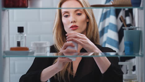 View-Through-Bathroom-Cabinet-Of-Young-Woman-Taking-Medication-From-Container