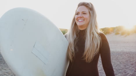 Woman-Wearing-Wetsuit-Holding-Surfboard-Enjoying-Surfing-Vacation-On-Beach-As-Sun-Sets