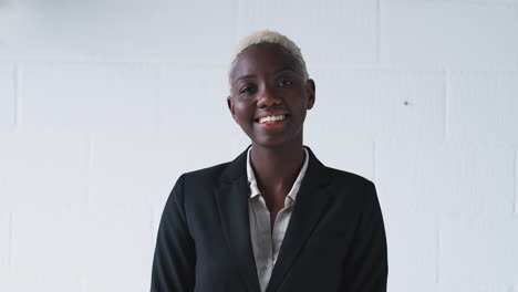 Portrait-Of-Smiling-Young-Businesswoman-Wearing-Suit-Standing-Against-White-Studio-Wall