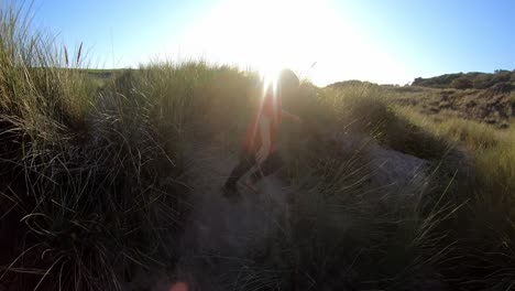 Rear-View-Of-Young-Boy-On-Beach-Vacation-Running-Through-Sand-Dunes-Against-Flaring-Sun