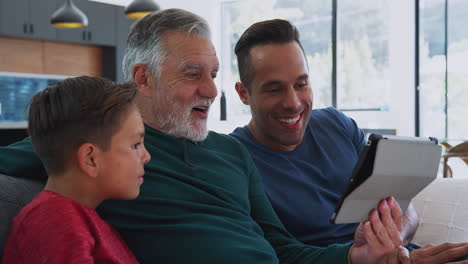 Männliche-Hispanische-Familie-Mit-Mehreren-Generationen-Sitzt-Zu-Hause-Auf-Dem-Sofa-Und-Schaut-Sich-Einen-Film-Auf-Einem-Digitalen-Tablet-An