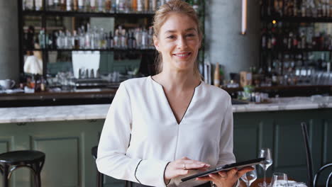 Portrait-Of-Female-Owner-Of-Restaurant-Bar-Standing-At-Counter-Using-Digital-Tablet