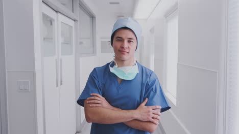 Portrait-Of-Male-Surgeon-Wearing-Scrubs-And-Mask-Standing-In-Hospital-Corridor