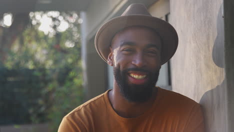 Retrato-De-Un-Hombre-Afroamericano-Sonriente-Con-Sombrero-En-El-Jardín-De-Casa-Contra-El-Sol-Abrasador
