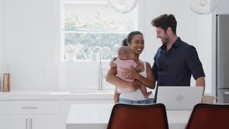 Family-With-Baby-Daughter-In-Kitchen-Using-Laptop-On-Counter