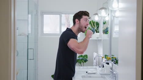 Man-Wearing-Pyjamas-Standing-At-Sink-Brushing-Teeth-In-Bathroom