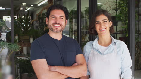 Portrait-Of-Male-And-Female-Owners-Of-Florists-Standing-In-Doorway-Surrounded-By-Plants