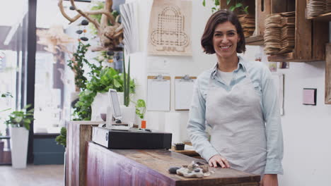 Portrait-Of-Smiling-Female-Sales-Assistant-Standing-Behind-Sales-Desk-Of-Florists-Store