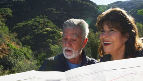 Senior-Hispanic-Couple-Looking-At-Map-As-They-Hike-Along-Trail-In-Countryside-Together