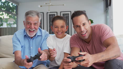 Männliche-Hispanische-Familie-Mit-Mehreren-Generationen,-Die-Zu-Hause-Videospiele-Spielt-Und-Zusammen-Auf-Dem-Sofa-Sitzt