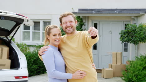 Portrait-Of-Couple-Holding-Keys-Outside-New-Home-On-Moving-Day-Unloading-Boxes-From-Car