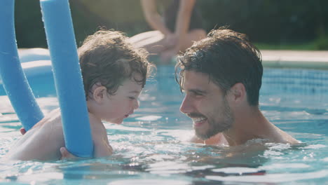 Father-Teaching-Son-To-Swim-On-Summer-Vacation-In-Outdoor-Swimming-Pool-With-Floatation-Aid