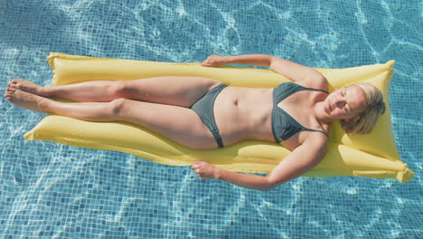 Overhead-Shot-Of-Woman-In-Bikini-Floating-And-Sunbathing-On-Inflatable-Airbed-In-Swimming-Pool