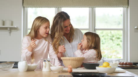 Mother-And-Two-Daughters-Wearing-Pyjamas-Baking-In-Kitchen-At-Home-Together