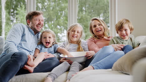 Familie-Sitzt-Zu-Hause-Auf-Dem-Sofa,-Lacht-Und-Schaut-Zusammen-Mit-Popcorn-Fern