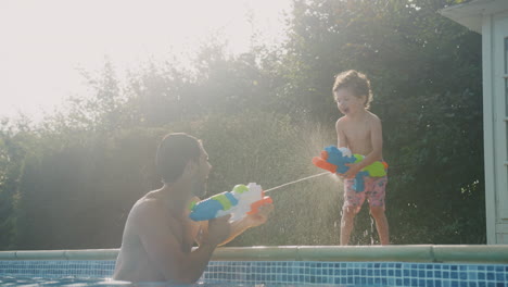 Vater-Und-Sohn-Bespritzen-Sich-Gegenseitig-Mit-Wasserpistolen-Und-Spielen-Im-Sommerurlaub-Im-Schwimmbad