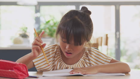 Junges-Asiatisches-Mädchen,-Das-Zu-Hause-Unterrichtet-Und-Am-Tisch-In-Der-Küche-Arbeitet-Und-Während-Der-Sperrung-In-Ein-Buch-Schreibt