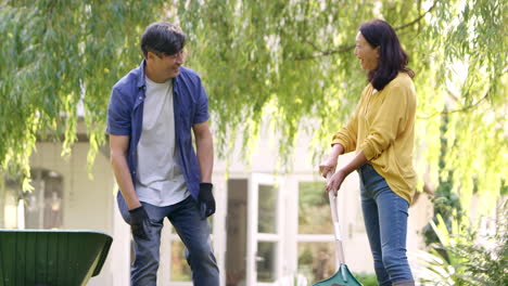 Mature-Asian-woman-raking-and-tidying-in-garden-as-husband-throws-leaves-that-he-has-picked-up-at-her---shot-in-slow-motion