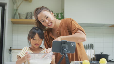 Asiatische-Mutter-Und-Tochter-Backen-Cupcakes-In-Der-Heimischen-Küche,-Während-Sie-Auf-Dem-Handy-Vloggen