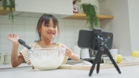 Asiatisches-Mädchen,-Das-Zu-Hause-In-Der-Küche-Cupcakes-Backt,-Während-Es-Auf-Dem-Handy-Vloggt