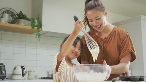 Asiatische-Mutter-Und-Tochter-Mischen-Zutaten,-Um-In-Der-Heimischen-Küche-Gemeinsam-Cupcakes-Zuzubereiten
