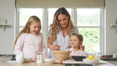 Mother-And-Two-Daughters-Wearing-Pyjamas-Baking-In-Kitchen-At-Home-Together