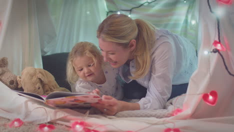 Mother-and-young-daughter-reading-story-in-homemade-camp-in-child's-bedroom-at-home---shot-in-slow-motion