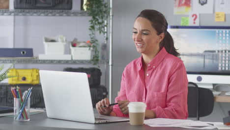 Geschäftsfrau-Im-Büro-Führt-Einen-Videoanruf-Am-Schreibtisch-Auf-Einem-Laptop-Durch-Und-Zeigt-Dem-Kunden-Entwürfe