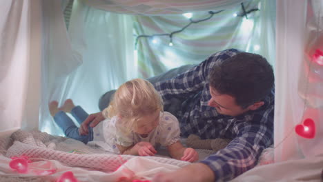 Father-and-young-daughter-reading-story-in-homemade-camp-in-child's-bedroom-at-home---shot-in-slow-motion