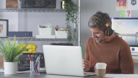 Geschäftsmann-Im-Büro,-Der-Musik-über-Kabellose-Kopfhörer-Hört-Und-Lufttrommeln-Spielt,-Während-Er-Einen-Laptop-Benutzt