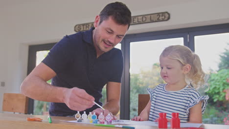 Father-and-young-daughter-having-fun-at-home-sitting-at-table-and-painting-decoration-together---shot-in-slow-motion