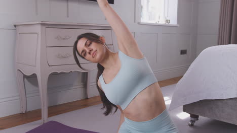 Woman-doing-yoga-joining-hands-together-before-stretching-sitting-on-exercise-mat-in-bedroom-at-home---shot-in-slow-motion