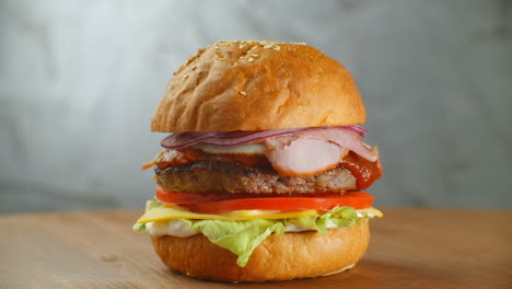 Der-Hamburger-Dreht-Sich-Auf-Einem-Holzbrett.-Ein-Burger-Mit-Schnitzel,-Salat,-Käse-Und-Tomaten-Dreht-Sich-Vor-Einer-Grauen-Wand