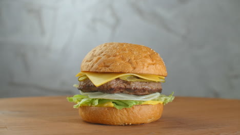 Der-Hamburger-Dreht-Sich-Auf-Einem-Holzbrett.-Ein-Burger-Mit-Schnitzel,-Salat,-Käse-Und-Tomaten-Dreht-Sich-Vor-Einer-Grauen-Wand