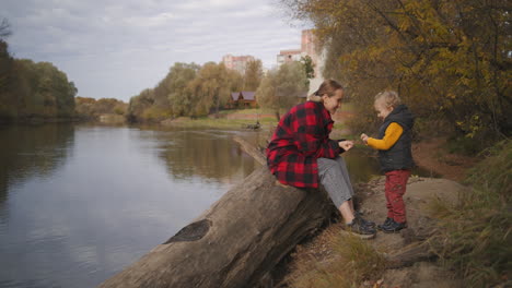 Descanso-Familiar-En-El-Parque-En-El-Día-De-Otoño-La-Joven-Madre-Está-Jugando-Con-Su-Pequeño-Hijo-En-La-Orilla-Del-Río-En-El-Bosque-Familia-Feliz-Y-Gente-Amorosa