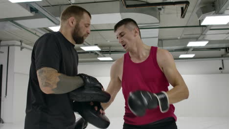 Two-men-in-a-white-gym.-The-coach-and-the-fighter-work-out-the-kick-in-the-jump-knee-on-the-paws-in-slow-motion