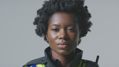 Studio-Portrait-Of-Smiling-Young-Female-Police-Officer-Against-Plain-Background