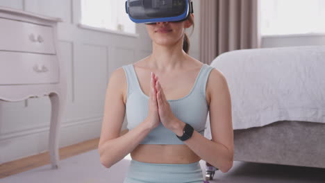 Kippende-Aufnahme-Einer-Frau,-Die-Auf-Einer-Yogamatte-Sitzt-Und-Ein-Virtual-Reality-Headset-Im-Heimischen-Schlafzimmer-Trägt-Und-An-Einem-Virtuellen-Unterricht-Teilnimmt-–-Aufgenommen-In-Zeitlupe