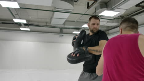 Cámara-Lenta:-Golpe-De-Potencia-A-La-Pata-De-Boxeo.-Fuerte-Atleta-Tatuado-En-Ropa-Deportiva-Entrenando-En-Patas-De-Boxeo-Con-Pareja