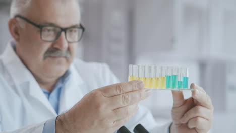 Científico-O-Tecnólogo-Realizando-Una-Prueba-De-Laboratorio.-Líquido-Concentrado.-Un-Químico-Masculino-Examina-Un-Matraz-Con-Una-Sustancia-Azul.-Sostiene-Un-Tubo-De-Ensayo-En-La-Mano-Y-Mezcla-El-Líquido-Del-Interior-Observando-La-Reacción-Química.-Imágenes-4k-De-Alta-Calidad