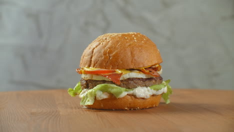 Toller-Burger-Mit-Rinderkotelett,-Tomaten,-Pilzen-Und-Gurken-Mit-Geschmolzenem-Käse-Dreht-Sich-Auf-Einem-Holzbrett-Auf-Hellem-Hintergrund.