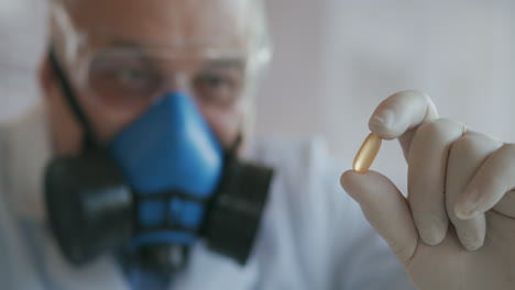 Primer-Plano-Extremo-De-Un-Científico-Con-Un-Respirador-Azul-Y-Gafas-Protectoras-Que-Desarrolló-Una-Vacuna-Contra-El-Coronavirus-Sosteniendo-Una-Pastilla-Blanca.-El-Médico-Examina-Los-Analgésicos-Y-Los-Medicamentos-Antivirales.-Vitaminas.-Imágenes-4k-De-Alta-Calidad