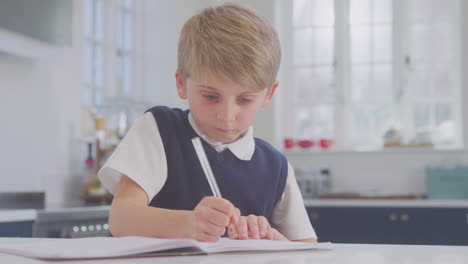 Boy-At-Home-Wearing-School-Uniform-Doing-Homework-On-Kitchen-Counter
