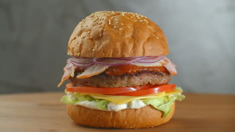 Great-Burger-with-beef-cutlet-tomatoes-mushrooms-and-cucumbers-with-melted-cheese-rotates-on-a-wooden-Board-on-light-background.