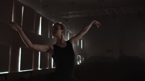 SLOW-MOTION:-prima-ballet-rehearses-a-solo-performance-standing-on-the-stage-of-the-theater-in-smoke-in-a-black-dress-in-the-light.